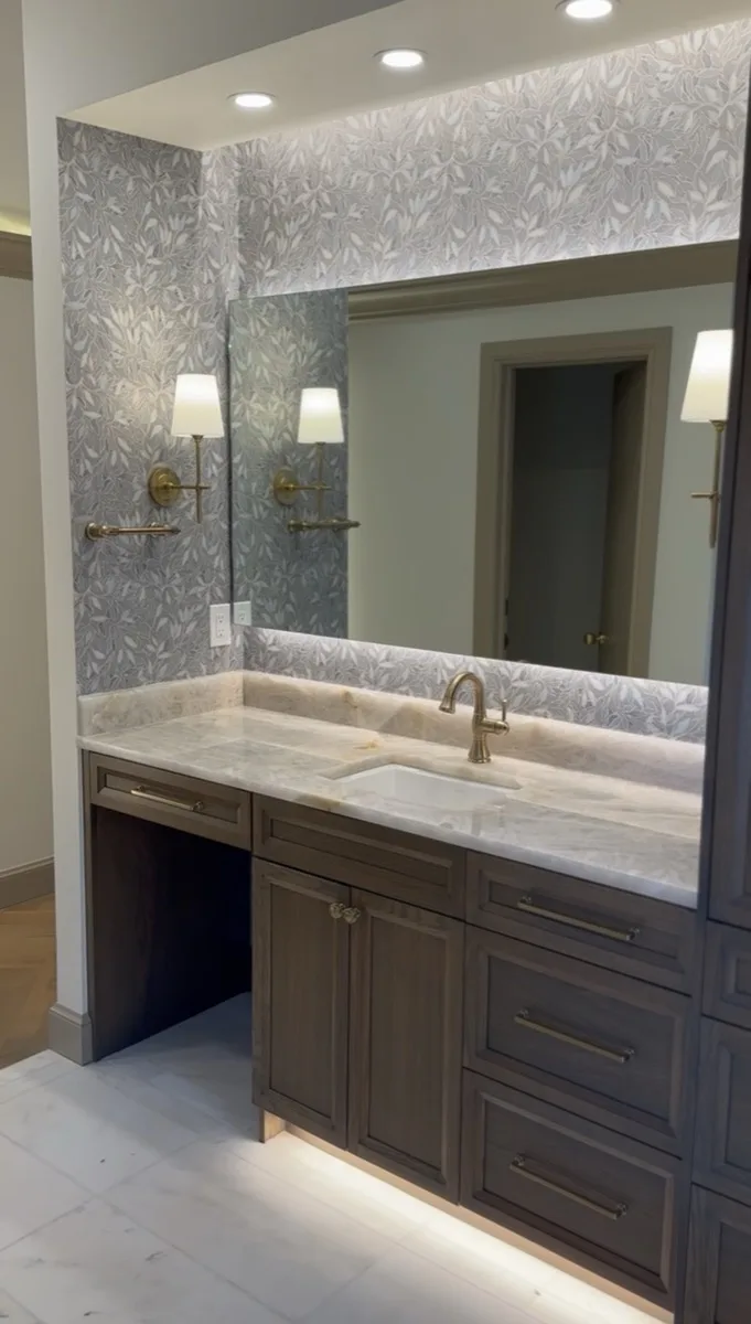 Bathroom vanity with floral wallpaper and brass sconce lighting in a home