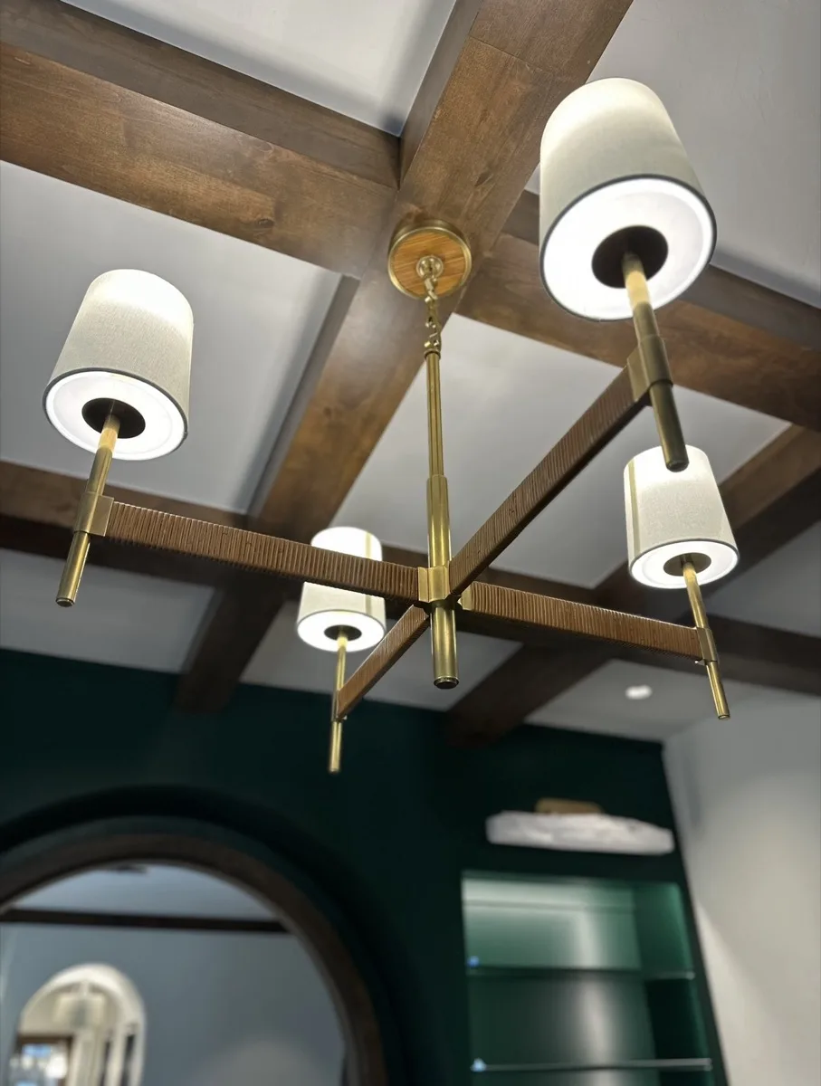 Brass drum shade chandelier under crossed wood beams in a home