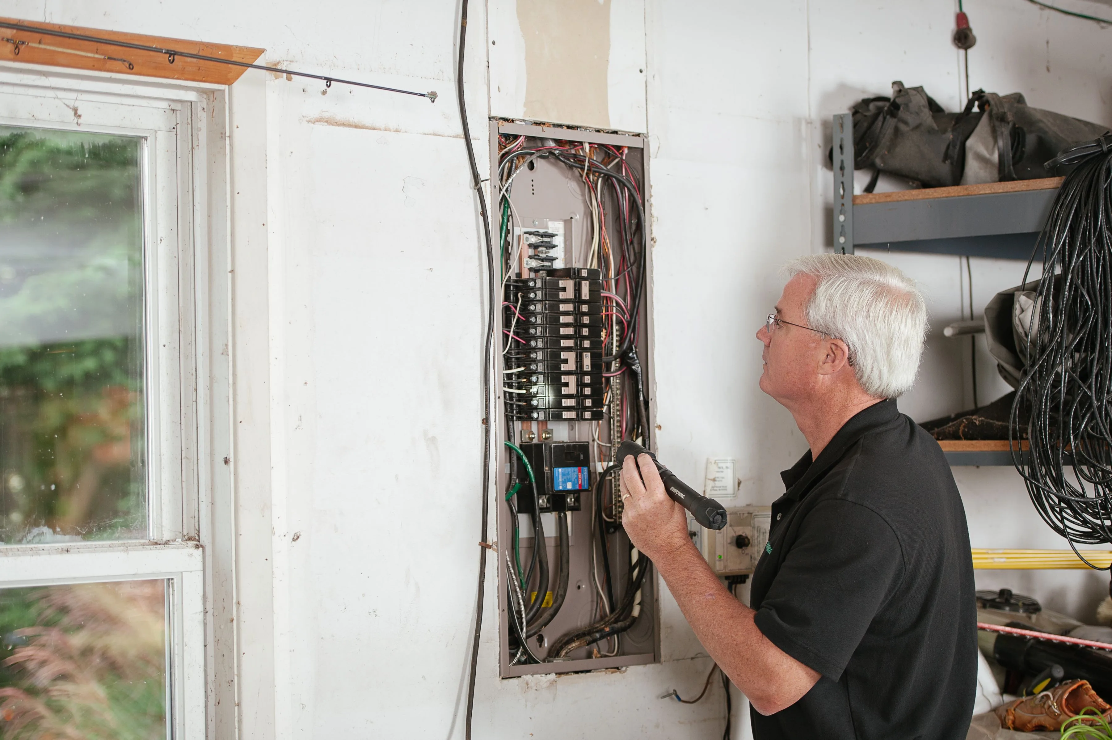 Electrician inspecting an open residential electrical panel with a flashlight
