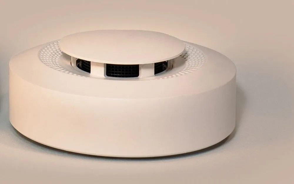 Modern round white smoke detector, disc-shaped with a vented top